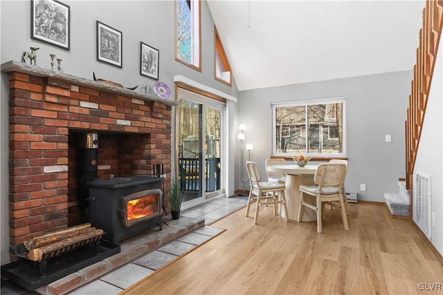 dining room with light wood-type flooring, high vaulted ceiling, and a wood stove