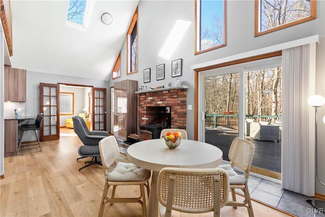 dining area with a wood stove, high vaulted ceiling, french doors, a skylight, and light hardwood / wood-style floors