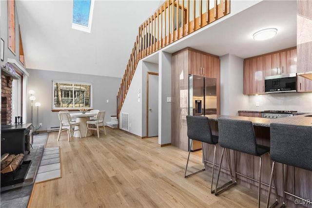 kitchen featuring a skylight, a breakfast bar, stainless steel appliances, high vaulted ceiling, and light hardwood / wood-style floors