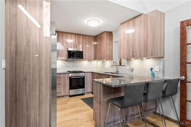 kitchen featuring kitchen peninsula, appliances with stainless steel finishes, dark stone counters, a breakfast bar, and sink