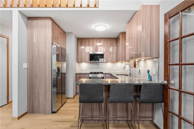 kitchen with sink, kitchen peninsula, light hardwood / wood-style floors, a breakfast bar area, and appliances with stainless steel finishes