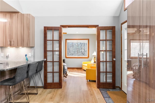 interior space with vaulted ceiling, light wood-type flooring, a healthy amount of sunlight, and french doors