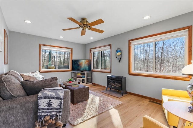 living room featuring a wood stove, ceiling fan, and light hardwood / wood-style flooring