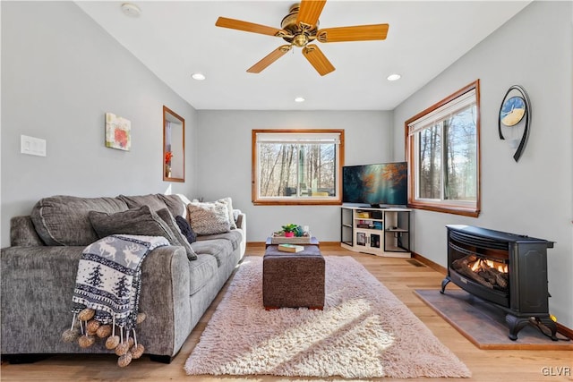 living room with light wood-type flooring, a wood stove, and ceiling fan