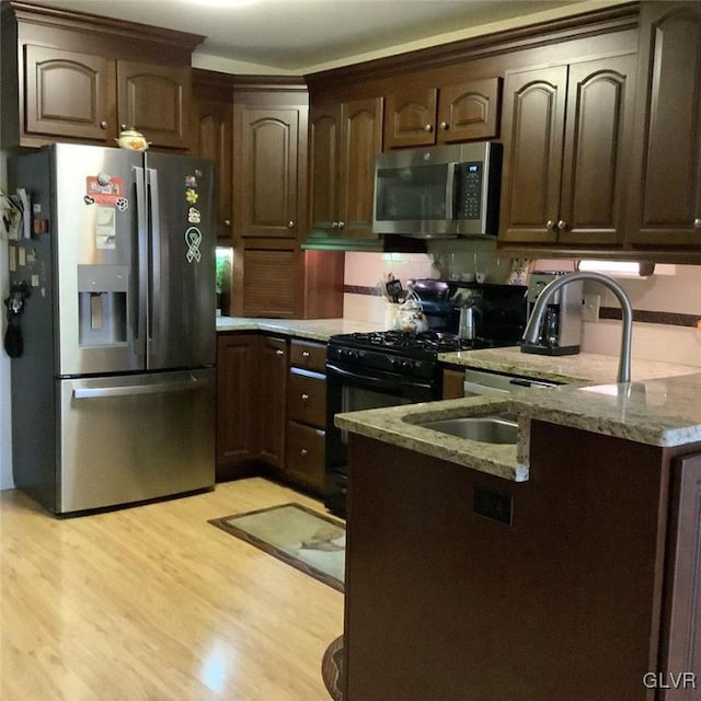 kitchen featuring light stone counters, dark brown cabinets, stainless steel appliances, and light wood-type flooring