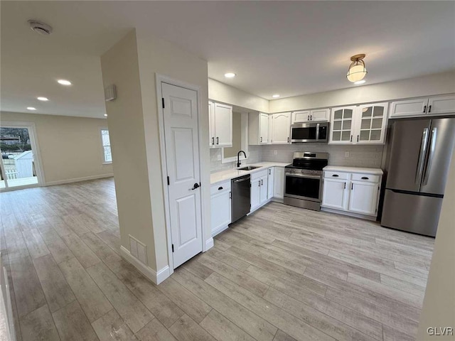 kitchen with backsplash, light hardwood / wood-style floors, sink, appliances with stainless steel finishes, and white cabinets