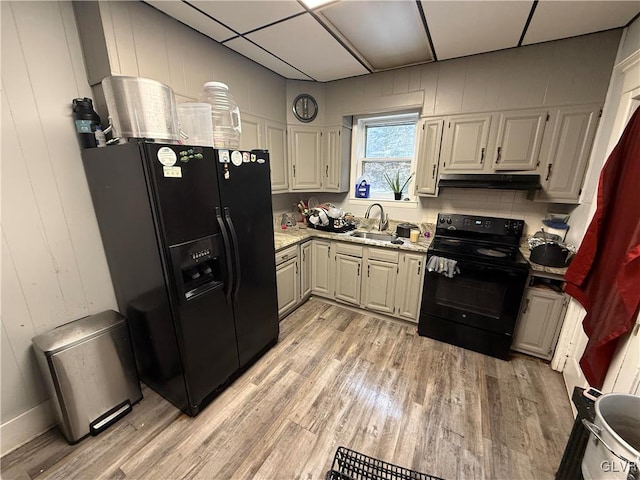 kitchen with black appliances, light stone counters, light wood-type flooring, and sink