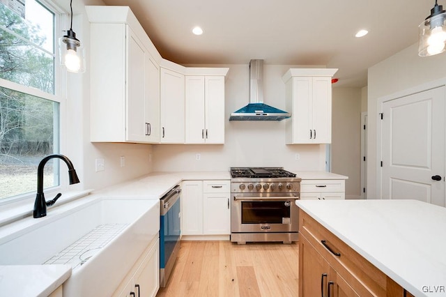 kitchen with stainless steel appliances, sink, decorative light fixtures, white cabinetry, and wall chimney range hood