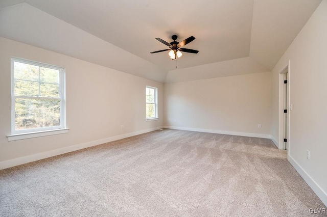 carpeted spare room with a raised ceiling, ceiling fan, and plenty of natural light