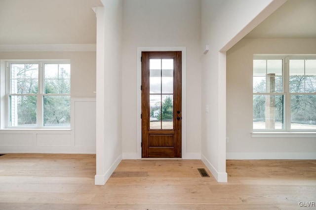 foyer with light wood-type flooring, crown molding, and a healthy amount of sunlight