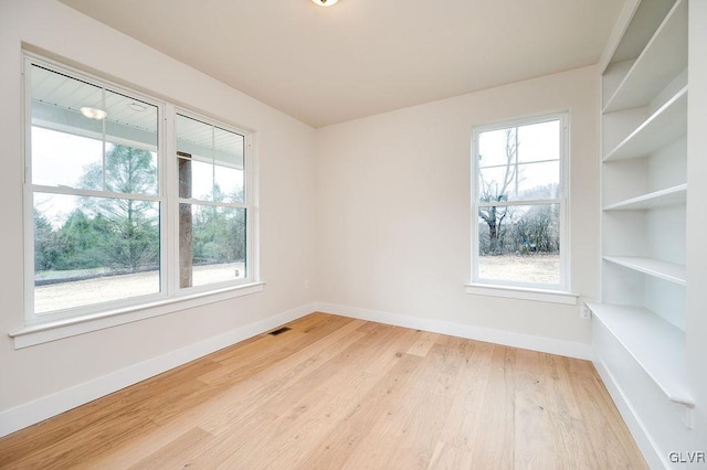 unfurnished room with light hardwood / wood-style flooring, a wealth of natural light, and built in shelves