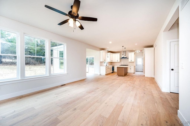 unfurnished living room featuring light wood-type flooring, ceiling fan, and sink