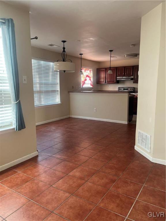 kitchen with kitchen peninsula, stove, decorative light fixtures, and dark tile patterned floors