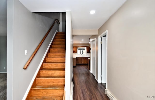 stairs with baseboard heating, wood-type flooring, and sink