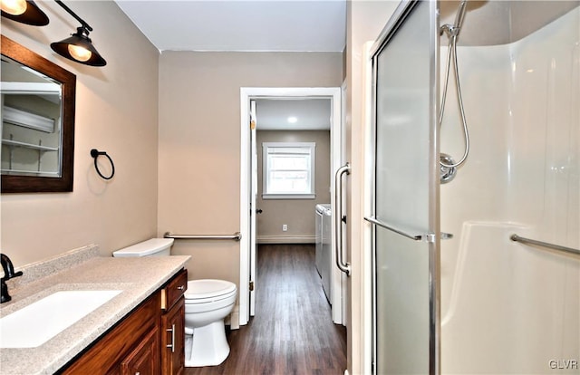 bathroom with toilet, vanity, washing machine and dryer, wood-type flooring, and an enclosed shower