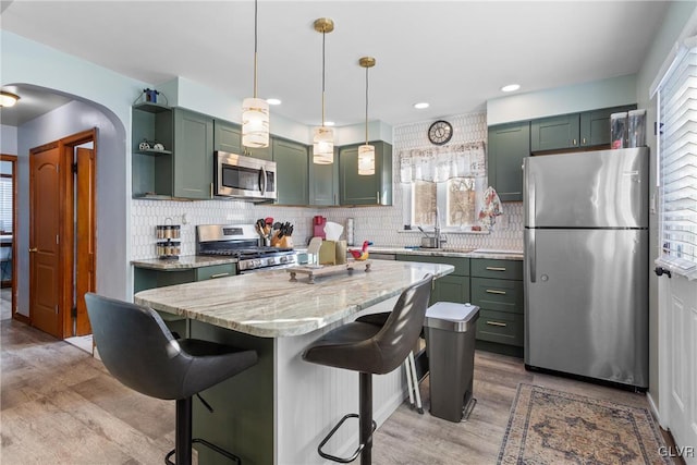 kitchen with appliances with stainless steel finishes, light stone counters, a breakfast bar, pendant lighting, and green cabinetry