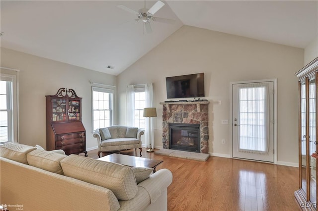 living room with ceiling fan, light hardwood / wood-style flooring, vaulted ceiling, and a fireplace