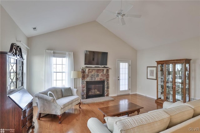 living room featuring vaulted ceiling, a fireplace, light wood-type flooring, and ceiling fan