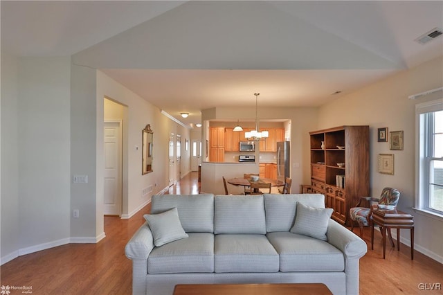 living room featuring vaulted ceiling, light hardwood / wood-style flooring, and a chandelier