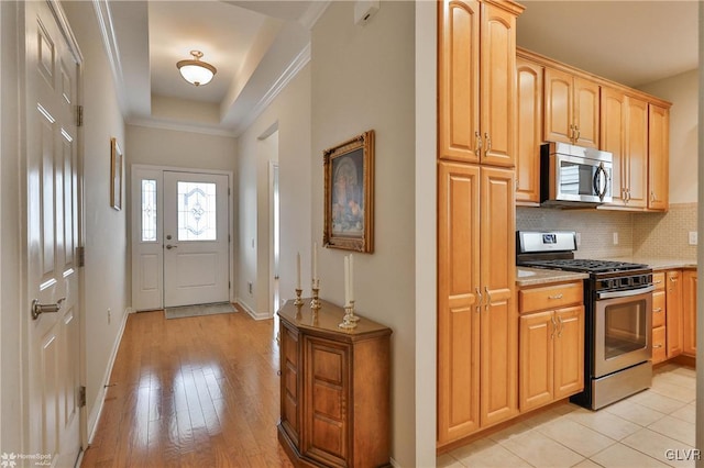 kitchen with light brown cabinets, light wood-type flooring, decorative backsplash, a tray ceiling, and appliances with stainless steel finishes