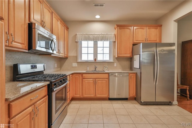 kitchen featuring light stone counters, stainless steel appliances, tasteful backsplash, and sink