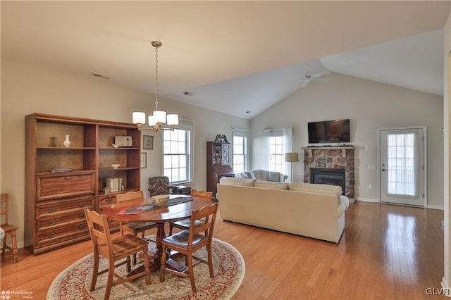 dining room featuring lofted ceiling, light hardwood / wood-style floors, a stone fireplace, and ceiling fan with notable chandelier