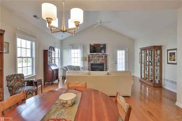 dining space with a healthy amount of sunlight, light wood-type flooring, ceiling fan with notable chandelier, and a fireplace