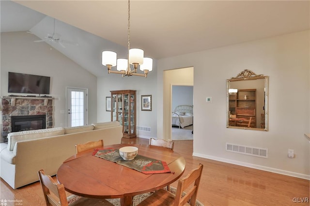 dining space featuring light hardwood / wood-style flooring, a stone fireplace, vaulted ceiling, and ceiling fan with notable chandelier