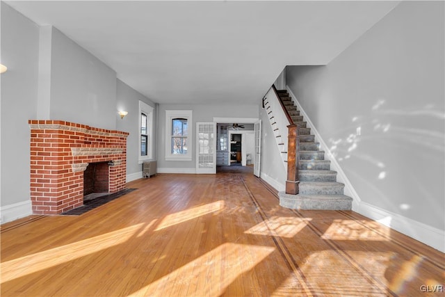 unfurnished living room featuring a brick fireplace, wood-type flooring, ceiling fan, and radiator heating unit