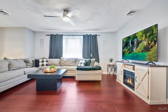 living room featuring ceiling fan, dark wood-type flooring, and a textured ceiling