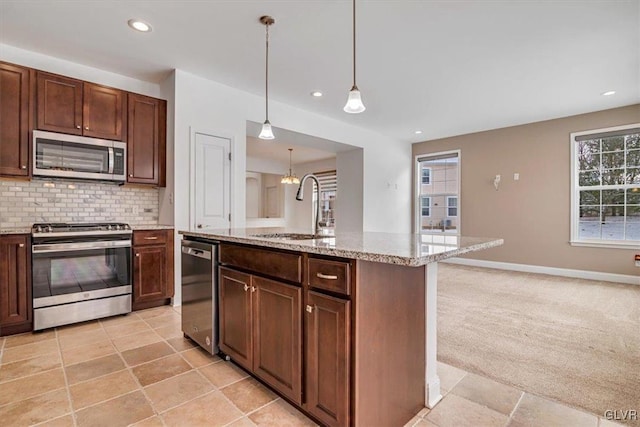 kitchen featuring stainless steel appliances, an island with sink, light stone countertops, sink, and decorative light fixtures