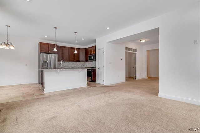 kitchen with decorative light fixtures, backsplash, a center island with sink, a breakfast bar, and appliances with stainless steel finishes