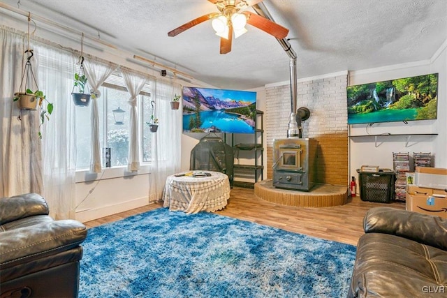 living room with wood-type flooring, a textured ceiling, ceiling fan, and a wood stove