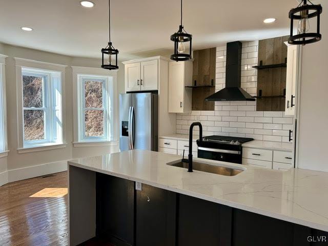 kitchen featuring stainless steel fridge, wall chimney exhaust hood, light stone countertops, white cabinetry, and pendant lighting