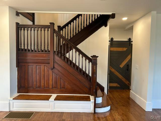 stairway featuring a barn door, baseboards, wood finished floors, and recessed lighting