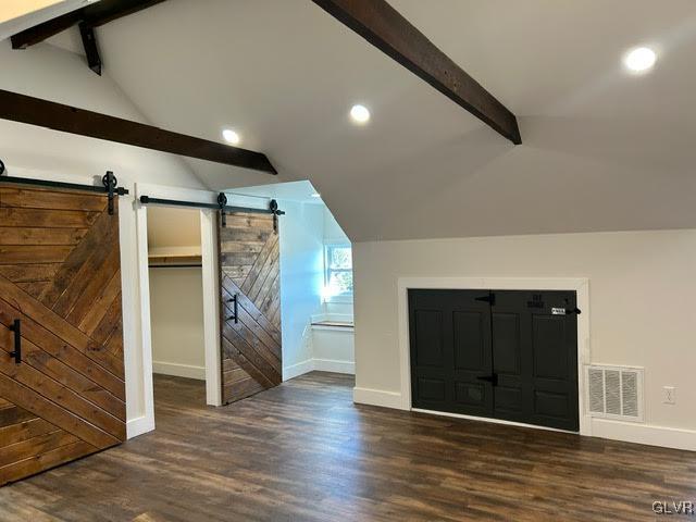 additional living space featuring vaulted ceiling with beams, a barn door, visible vents, baseboards, and dark wood-style floors