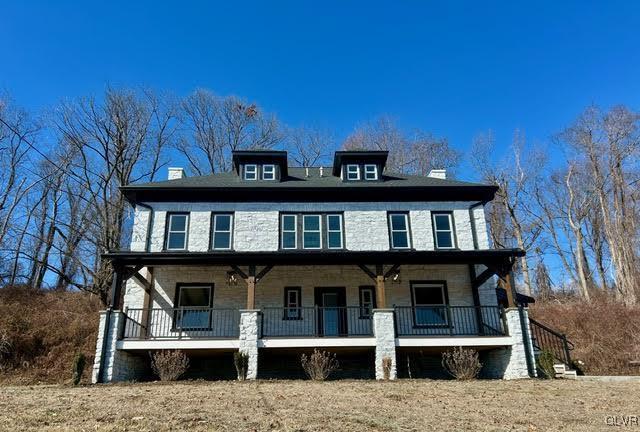 american foursquare style home with a porch, stone siding, and a chimney