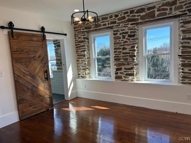 unfurnished dining area featuring baseboards, a barn door, dark wood finished floors, and a notable chandelier