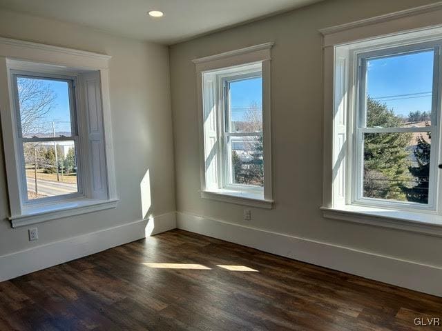 unfurnished room with dark wood-style floors, a wealth of natural light, and baseboards