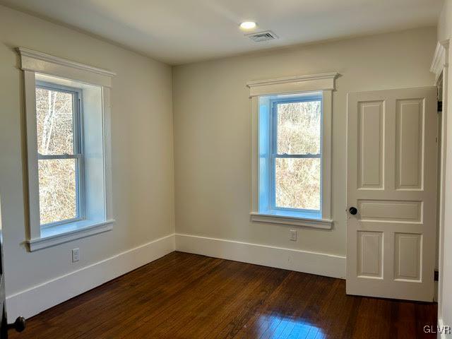 unfurnished room featuring visible vents, baseboards, and dark wood-style flooring