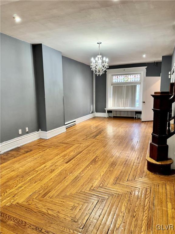 unfurnished living room with light parquet flooring, a notable chandelier, and radiator heating unit