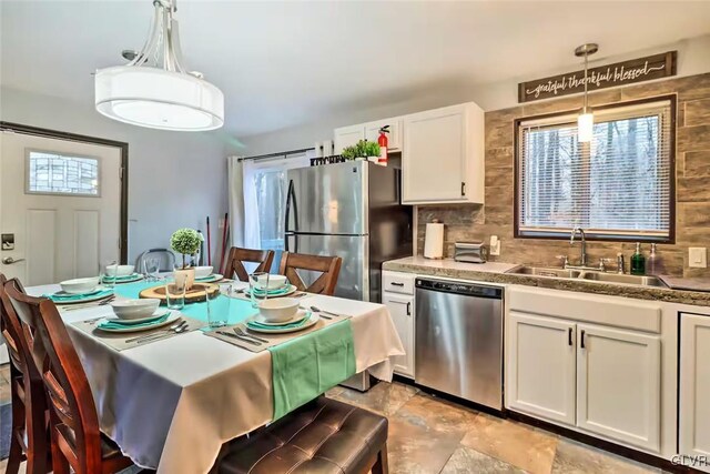 kitchen featuring stainless steel appliances, sink, decorative light fixtures, white cabinets, and backsplash