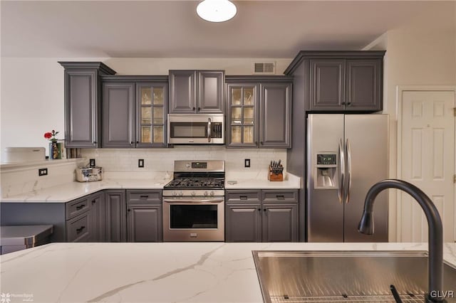 kitchen featuring light stone counters, appliances with stainless steel finishes, decorative backsplash, and sink