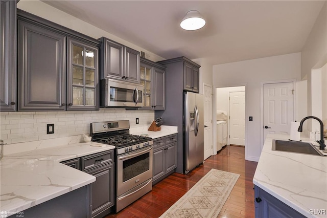 kitchen with gray cabinetry, stainless steel appliances, light stone countertops, dark hardwood / wood-style floors, and sink