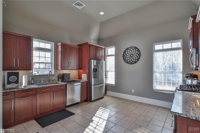 kitchen featuring appliances with stainless steel finishes, sink, stone countertops, light tile patterned flooring, and tasteful backsplash