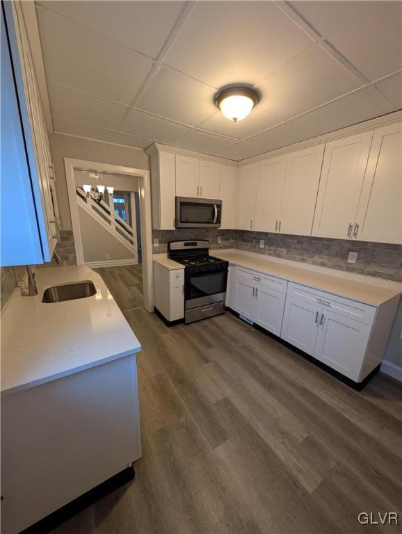 kitchen featuring stainless steel appliances, white cabinetry, decorative backsplash, dark hardwood / wood-style floors, and a notable chandelier