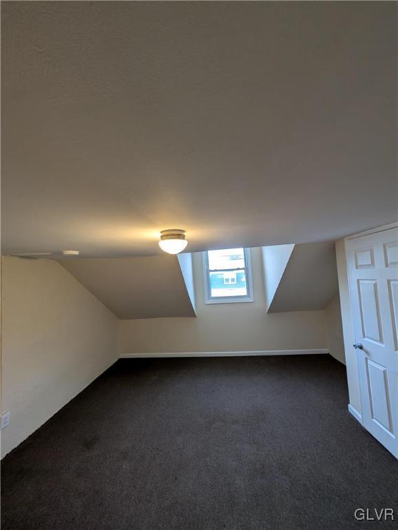 additional living space with dark colored carpet and lofted ceiling