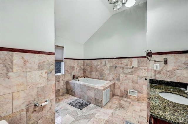 bathroom with tile walls, vanity, vaulted ceiling, and a relaxing tiled tub