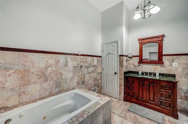 bathroom featuring tile walls, a chandelier, tiled tub, and vanity