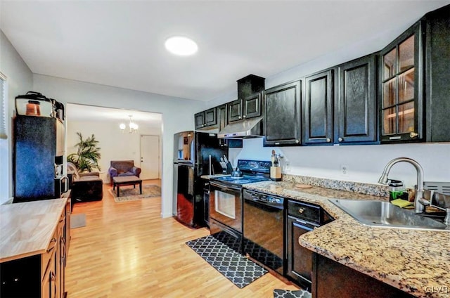 kitchen featuring sink, an inviting chandelier, light hardwood / wood-style flooring, light stone countertops, and black appliances